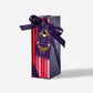 A boxed chocolate gift set with a dark navy rectangular package tied with a wide purple ribbon. Several red and pink chocolate bars are visible inside, along with a decorative purple hanging tag reading 'Cheese and Chocolate'.