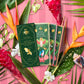 Three green chocolate packaging on a pink background with tropical flowers and leaves.