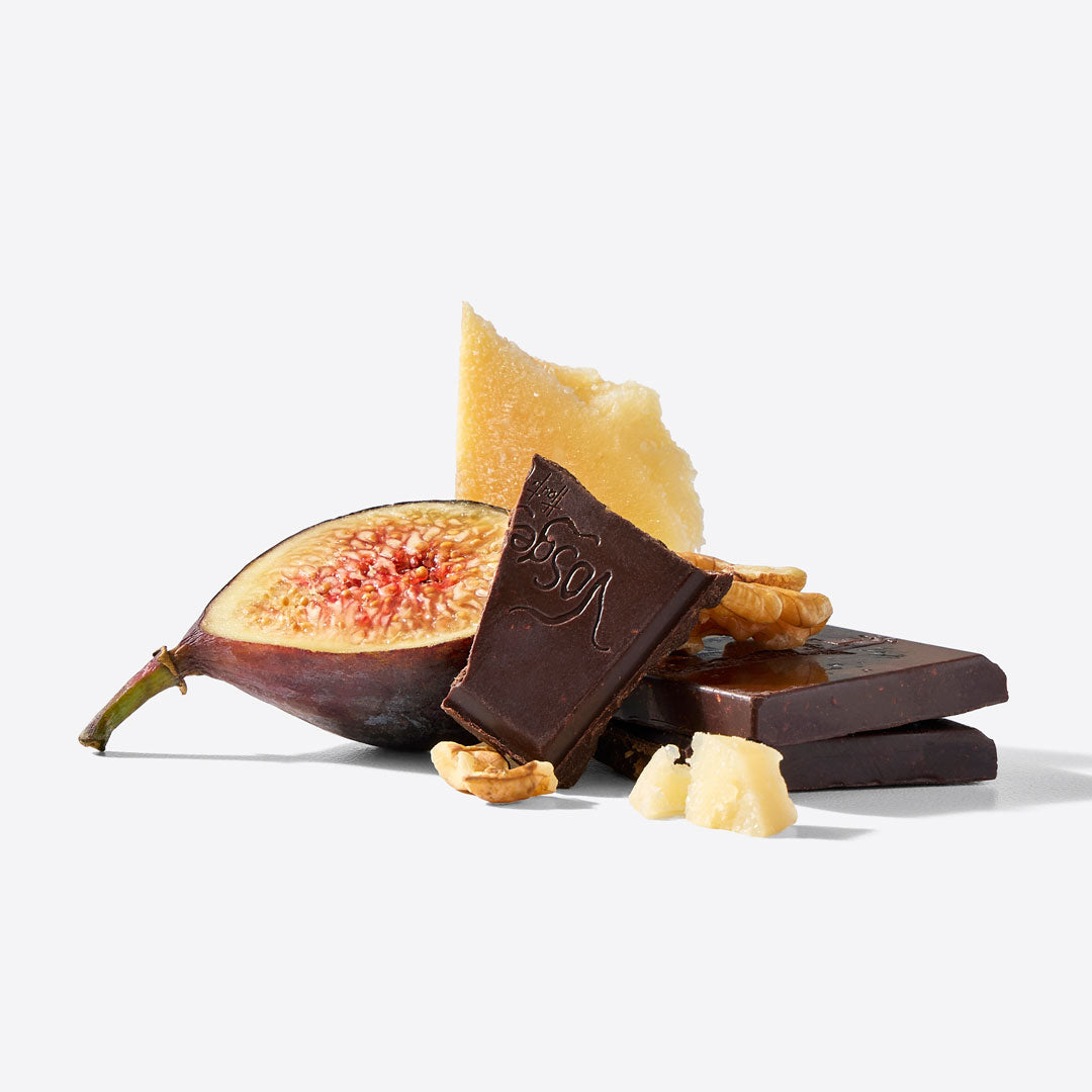 Dark chocolate bars and a halved fig with pale yellow wax or honey drizzle, arranged on a clean white background.