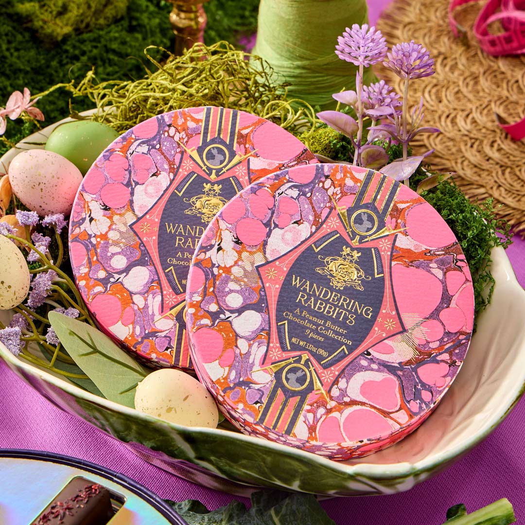 Two decorative tins with floral patterns on a table with Easter eggs and flowers.