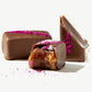 Close up of two Vosges caramels, one bitten displaying buttery caramel center and milk chocolate coating on a white background.