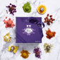 Purple Vosges Haut-Chocolat chocolate box tied with ribbon surrounded by fresh ingredients and exotic truffles on a marble slab.