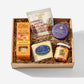 A curated gourmet gift box from Effie's and Albina City containing a box of oatcake biscuits, sweet and salty hazelnuts, truffles, a cheese wheel, and a jar of Gibrli 'Dirty' honey, arranged in a cardboard box with shredded paper.