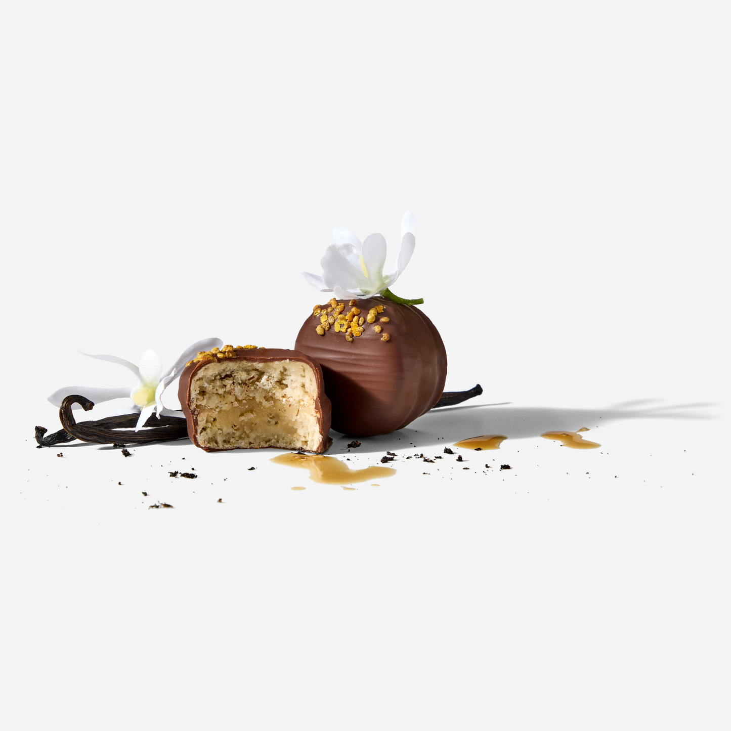 Chocolate-covered dessert with vanilla bean and white flowers on a white background