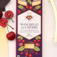 A 3 ounce Vosges Manchego and Cherry bar beside cheese a few cherries and pieces of chocolate on a white background