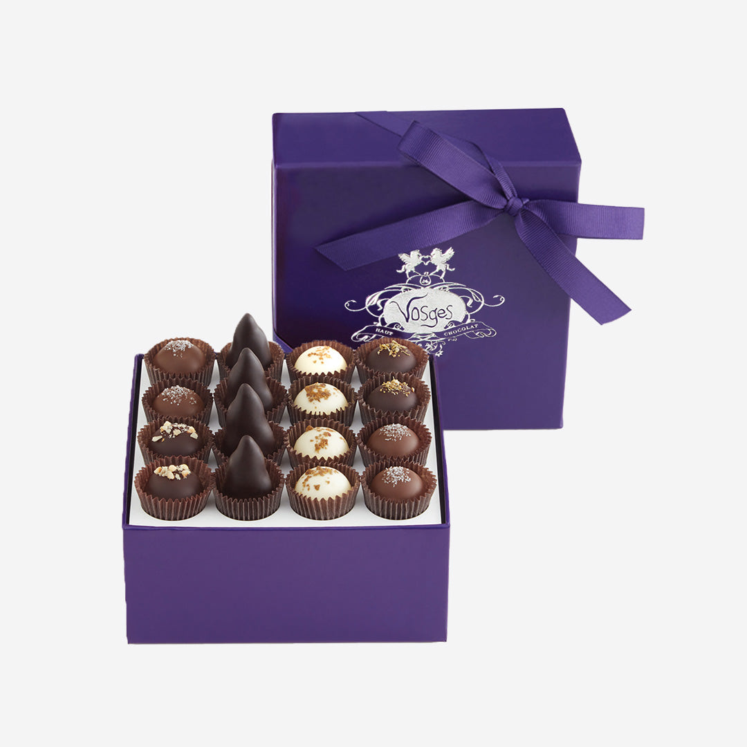 An open box of assorted chocolates displayed next to its purple lid, which features the 'Vosges' brand logo and a purple ribbon, on a light gray background.