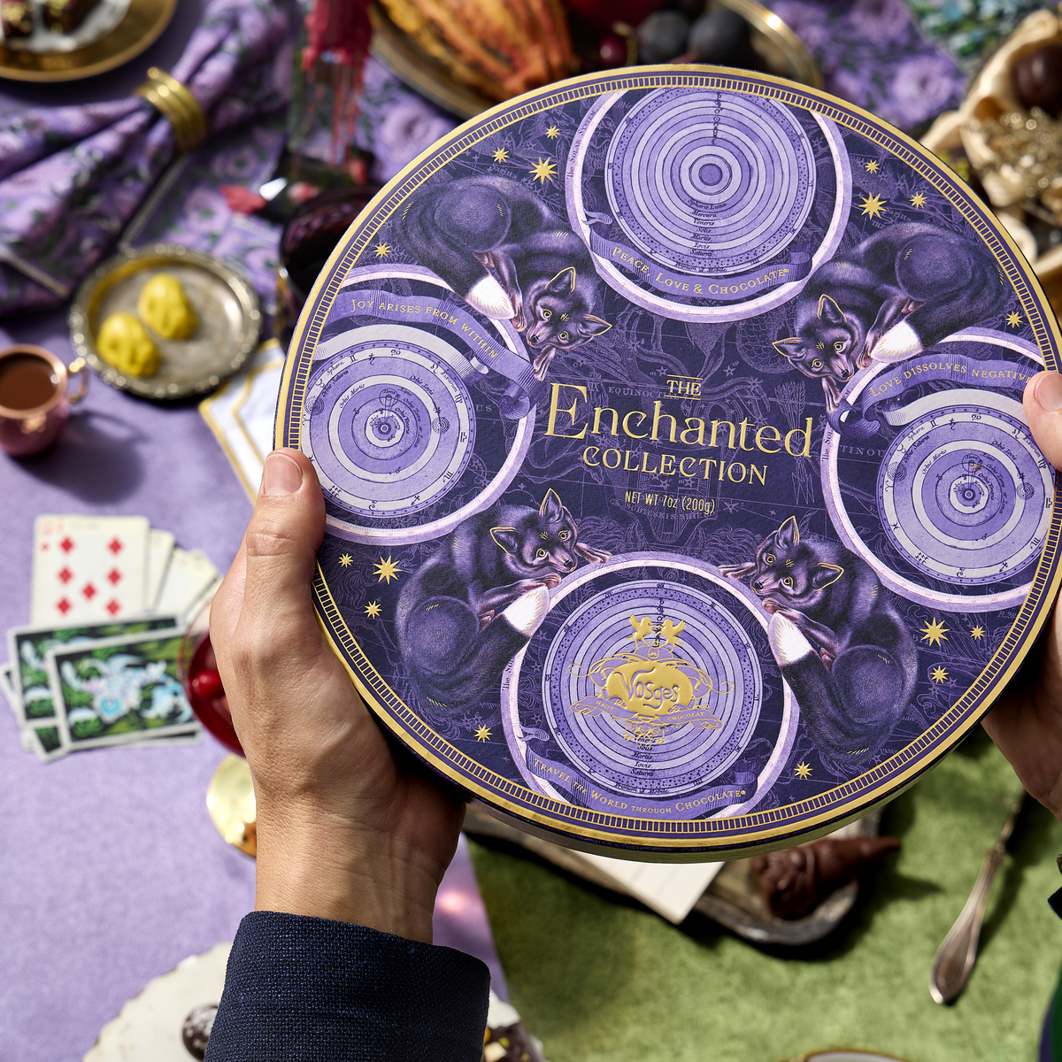 Hand holding Enchanted Magic Chocolate Tower tin featuring celestial purple artwork