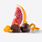 Enchanted Magic Chocolate Tower assortment featuring glossy dark chocolate truffles, orange zest curls, and a grapefruit slice behind.