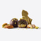 Enchanted Magic Chocolate Tower truffles with pistachio toppings and a cut-open center, arranged with almonds and a large leaf on a white background.