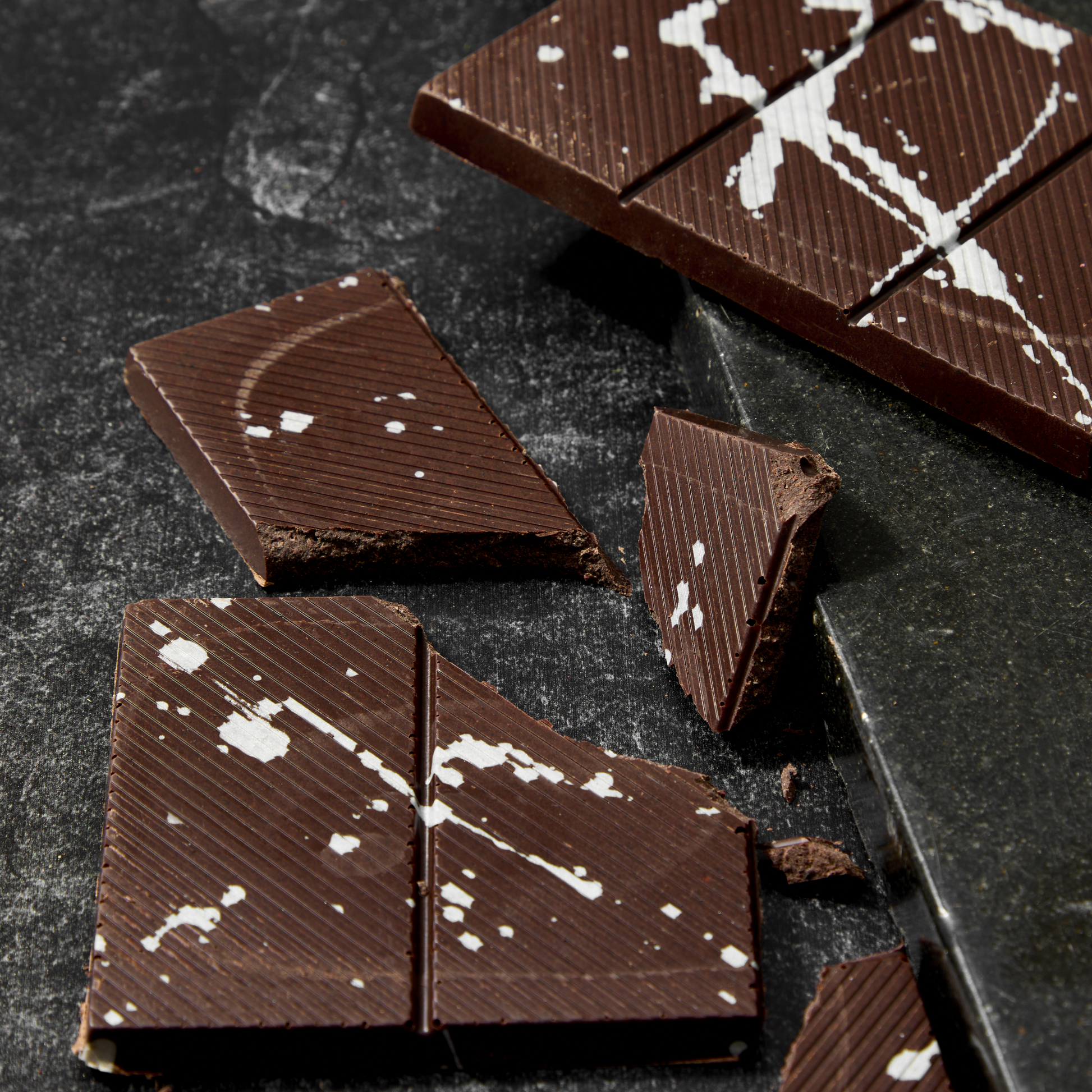Dark chocolate bars with white chocolate chips on a dark surface